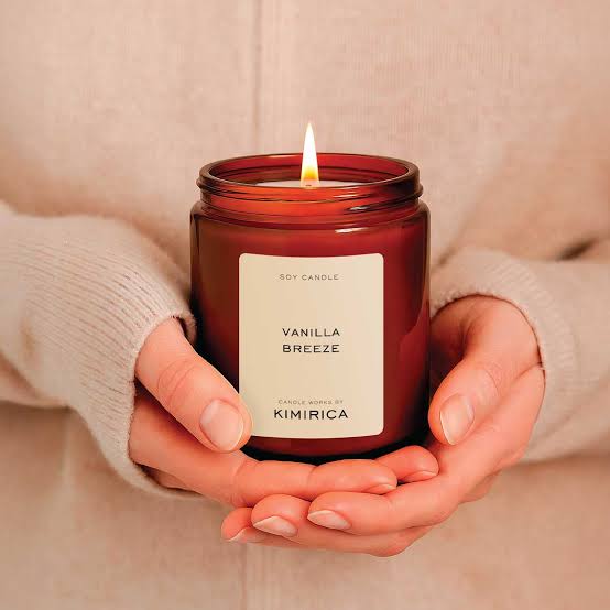 Vanilla scented candle in a glass jar held in hands creating a cozy and relaxing atmosphere 
